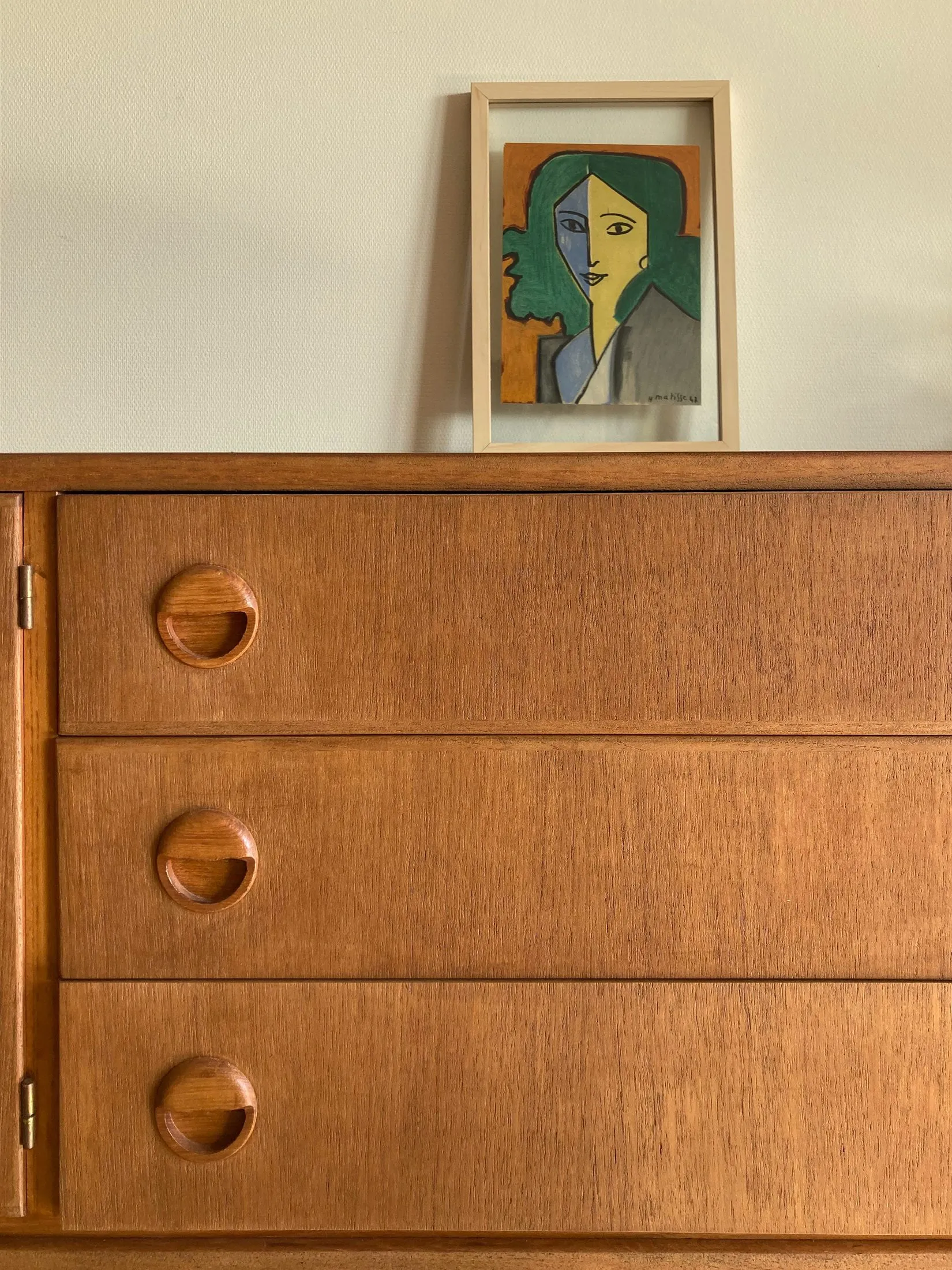 Commode en teck des années 50 surmontée d'un portrait graphique encadré