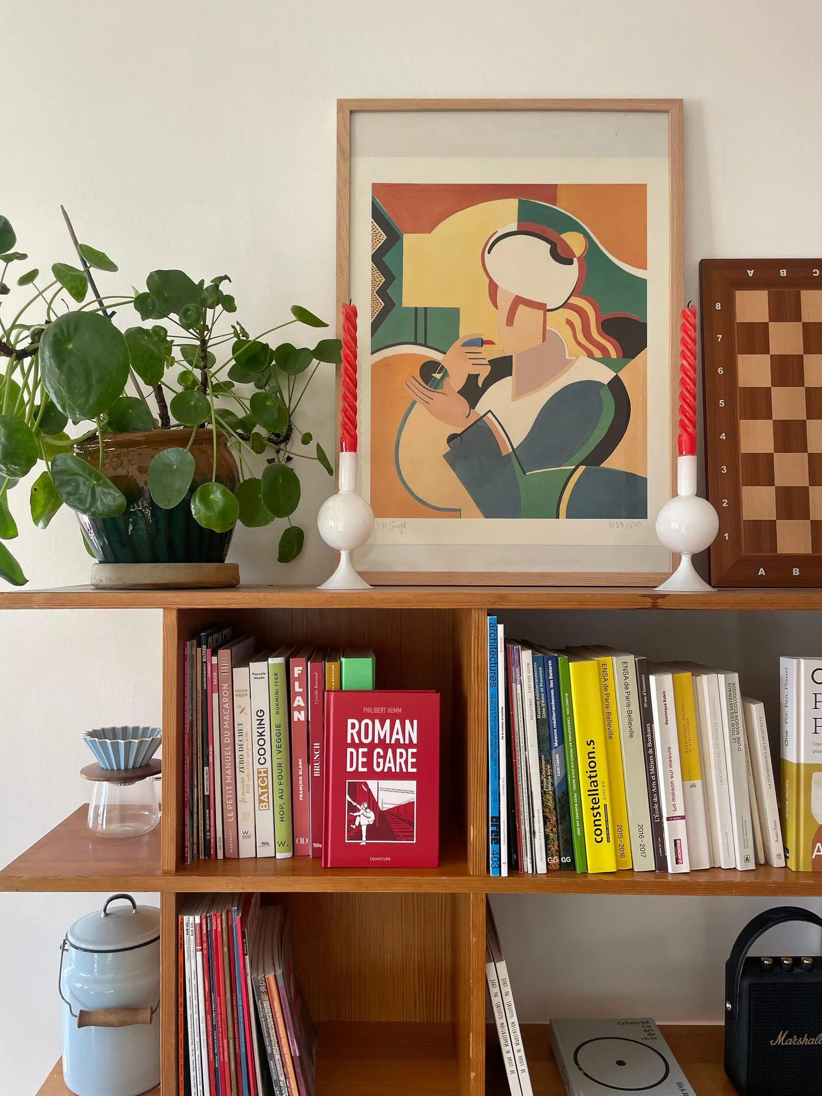 Étagère basse en bois garnie de livres et d'objets, affiche colorée posée au-dessus