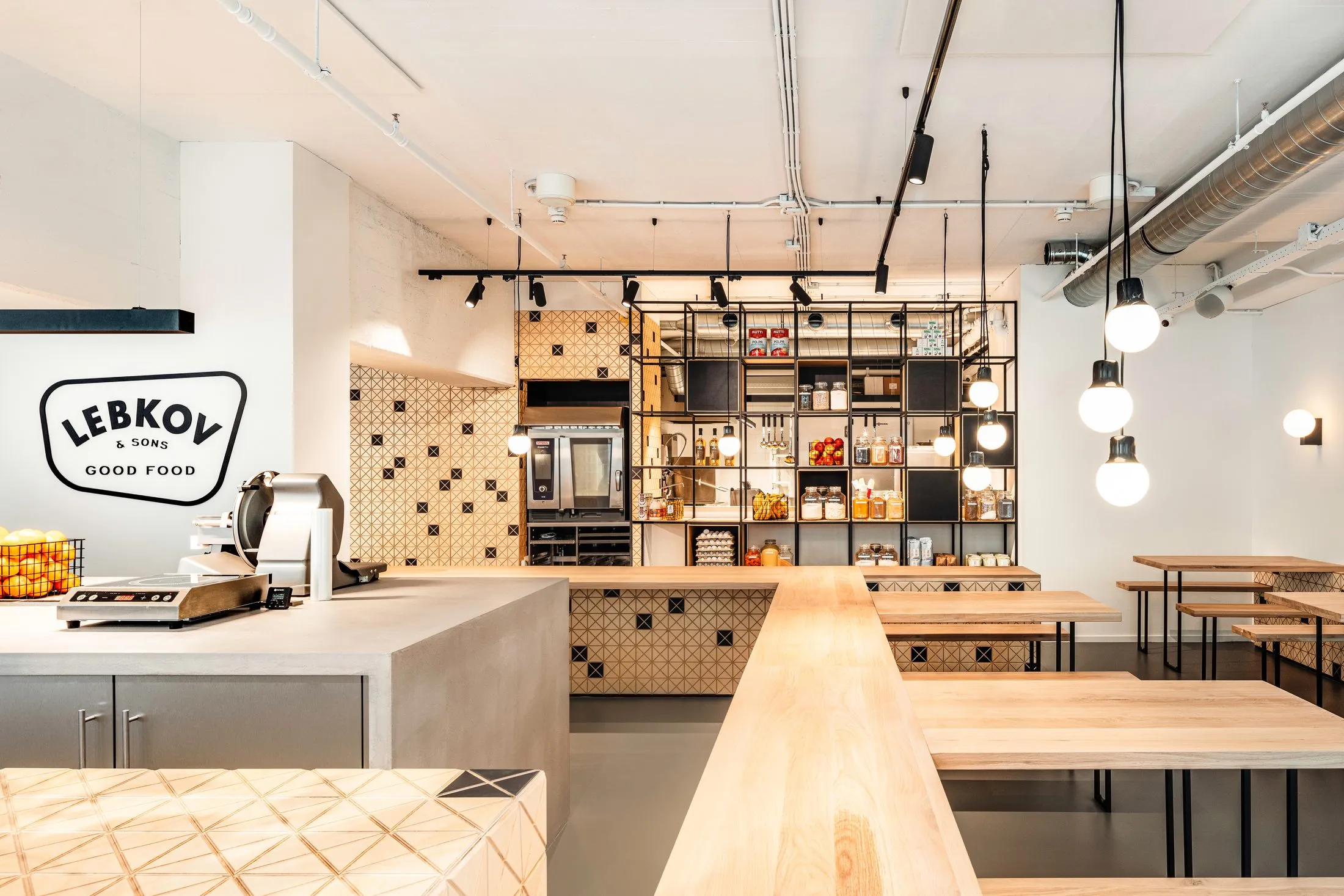 Salle du café : comptoir en bois clair, tables hautes et étagère noire toute hauteur