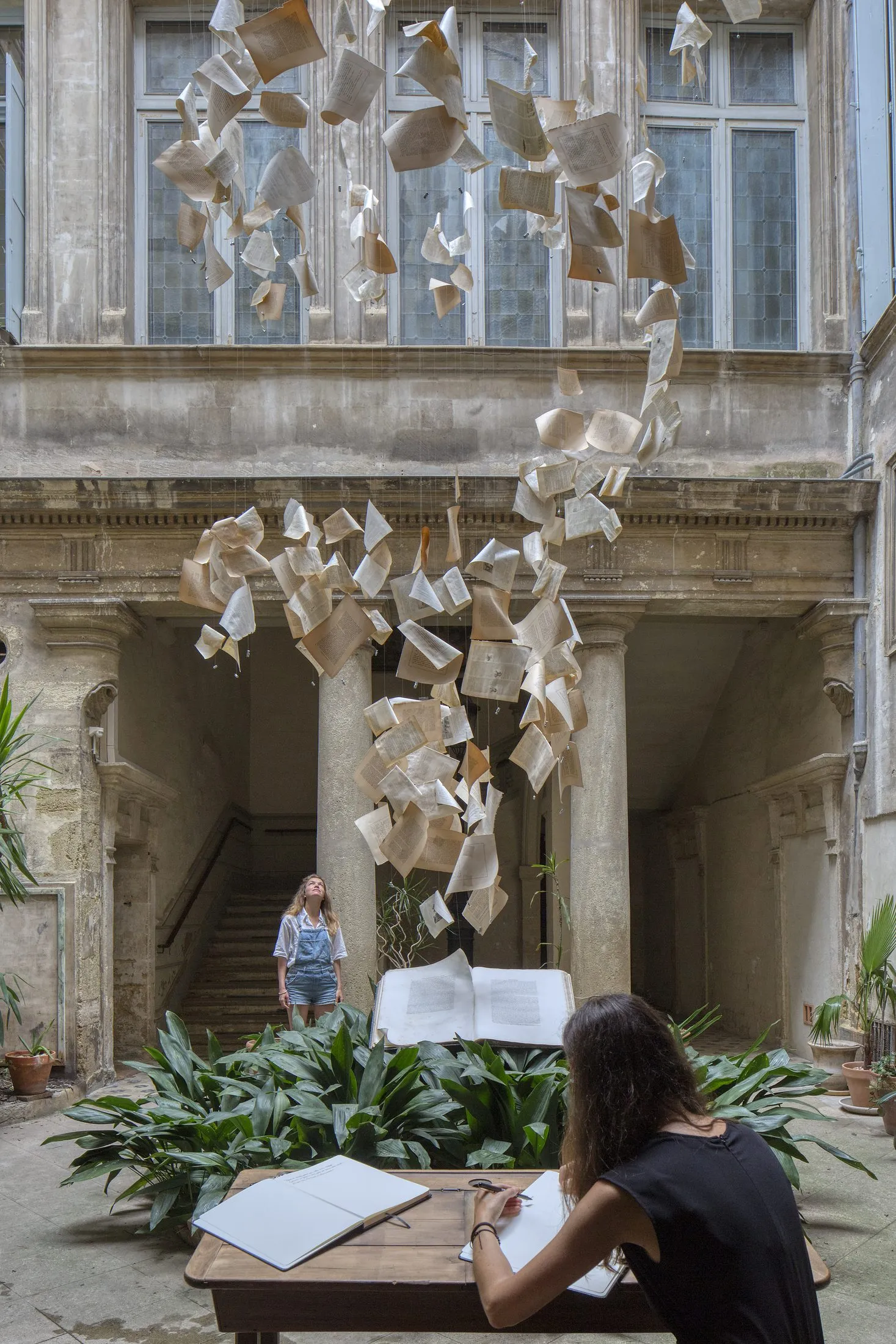Deux visiteuses écrivent au pupitre, sous l'installation de pages