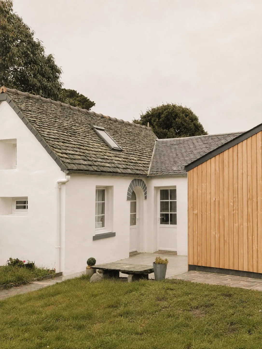 Maison blanche au toit d'ardoise et son extension en bardage bois, vues depuis le jardin