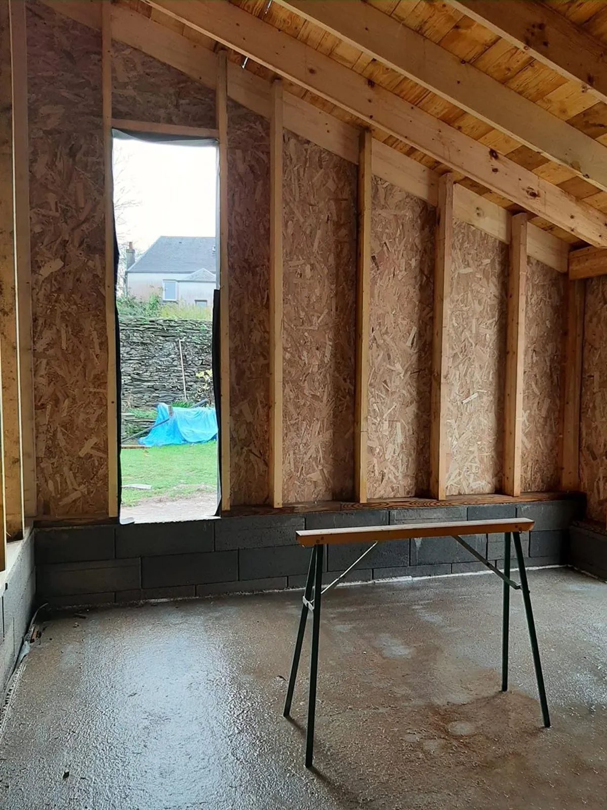 Chantier de l'extension : ossature bois et panneaux apparents, table de travail sur la dalle
