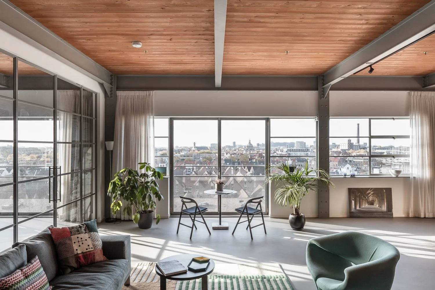 Séjour du loft : poutres métalliques, plafond en bois et baies ouvertes sur les toits de la ville