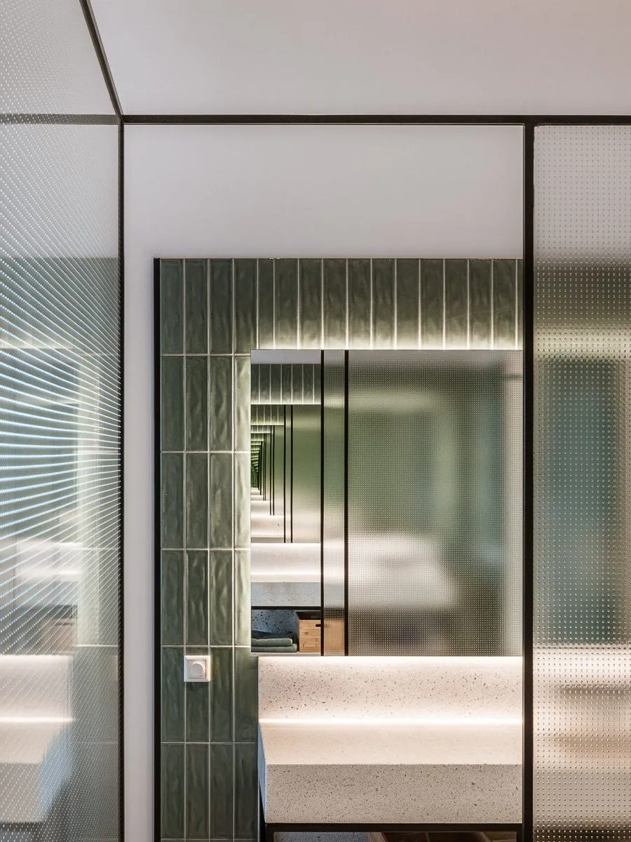 Verrière en verre texturé devant le miroir encadré de carreaux verts de la salle de bains