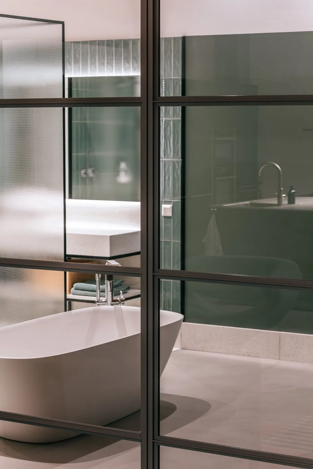 Baignoire îlot derrière une verrière noire, vasque suspendue en arrière-plan