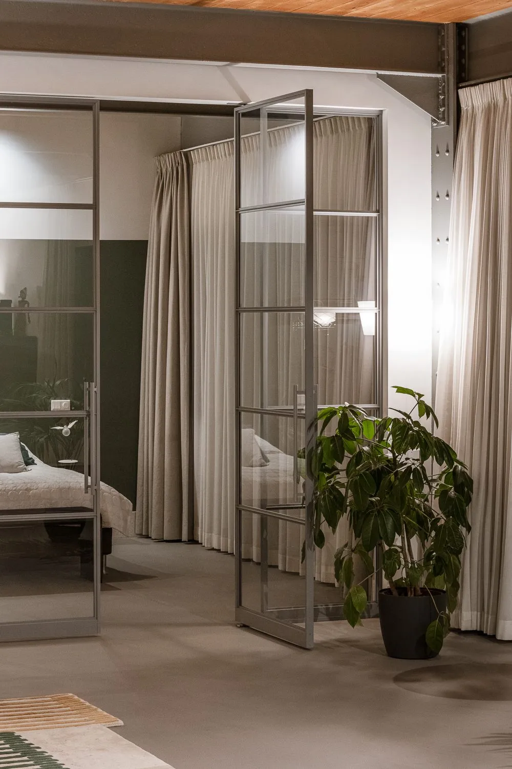 Chambre séparée du séjour par une verrière, grande plante au premier plan
