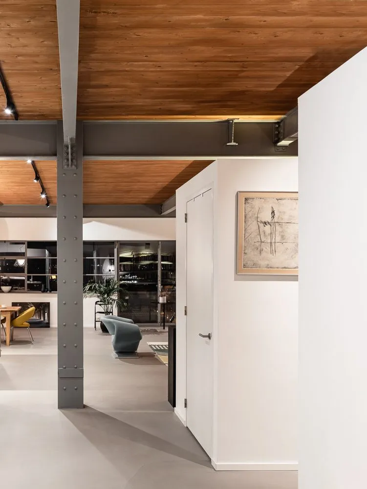 Couloir sous le plafond en bois, poteau métallique au premier plan et gravure encadrée au mur