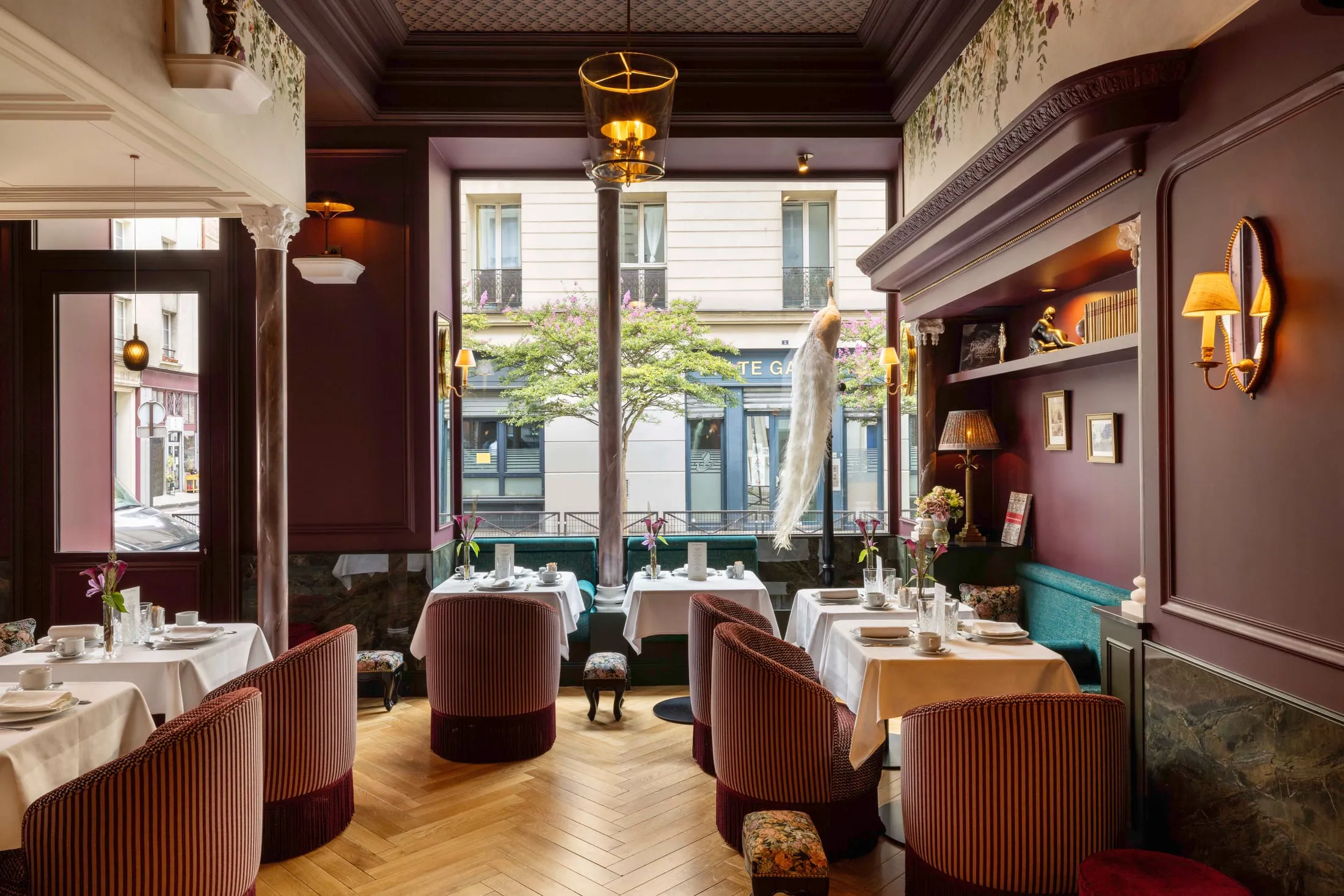 Salle du petit-déjeuner aux boiseries bordeaux, tables nappées de blanc et fauteuils en velours