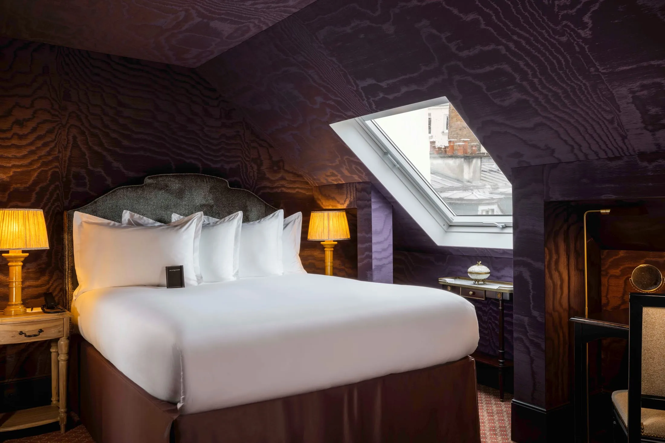 Chambre sous les toits aux murs sombres, lit blanc et lampes de chevet dorées