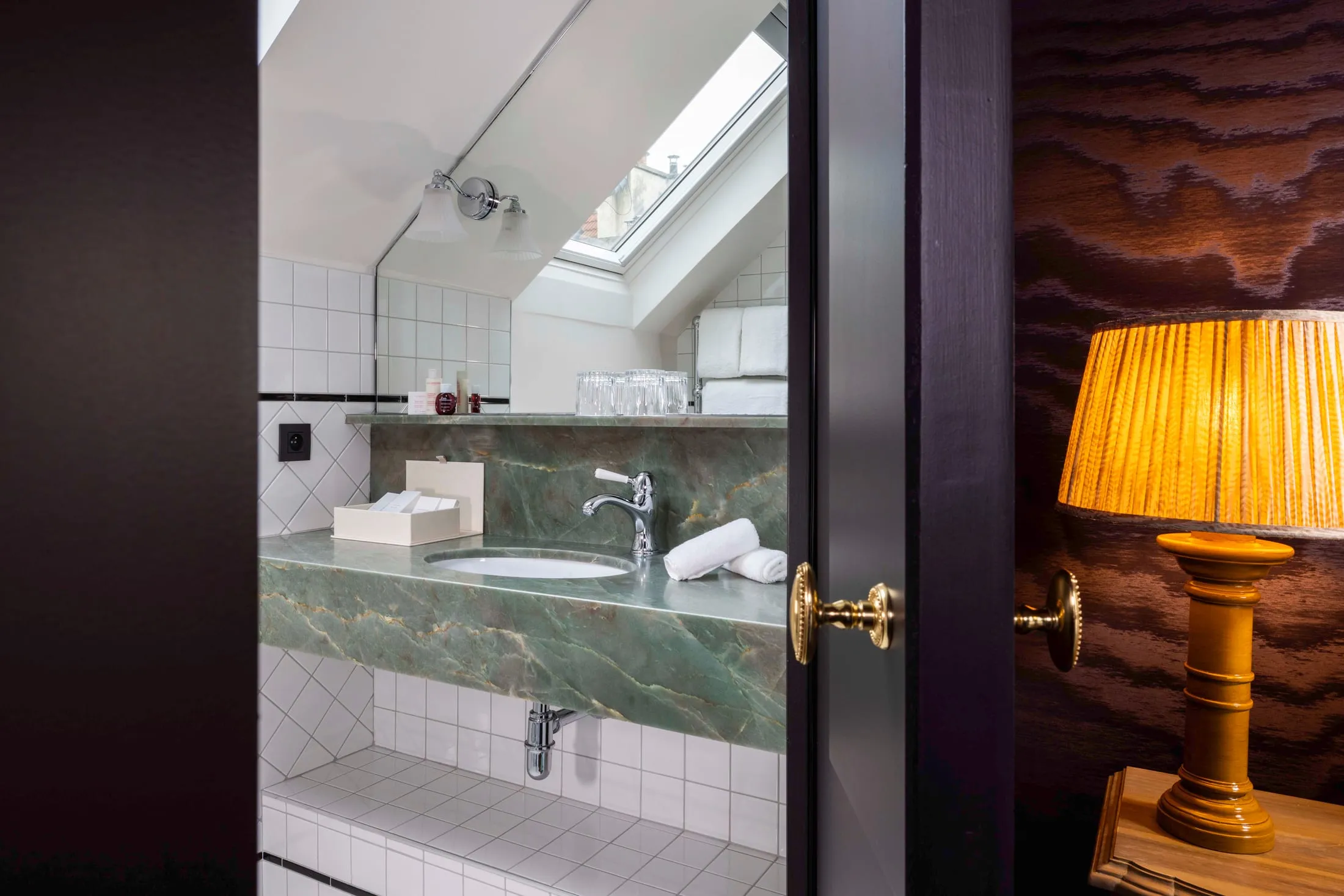 Salle de bains à vasque en marbre vert sous une fenêtre de toit, lampe à abat-jour plissé au premier plan