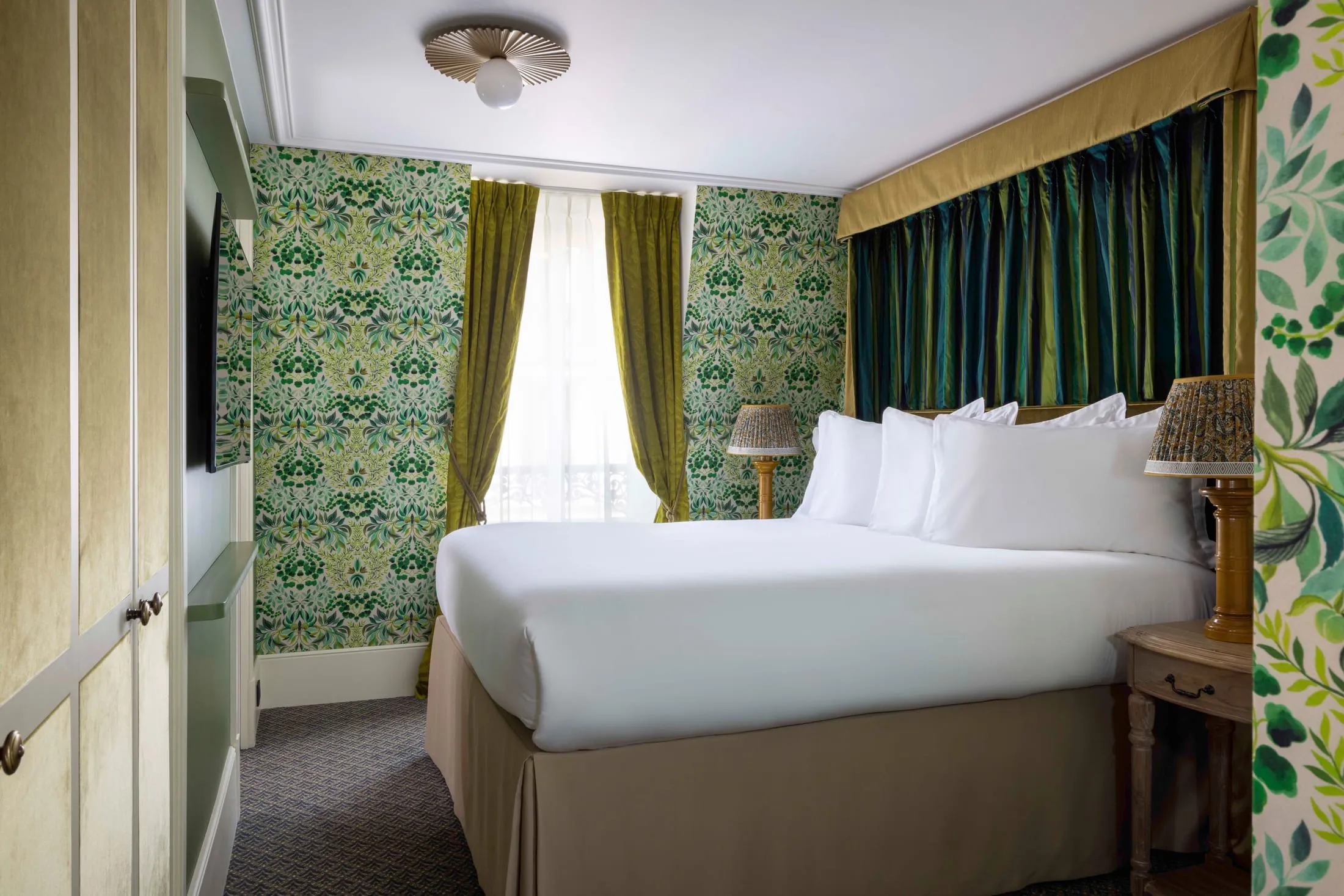 Chambre au papier peint végétal vert, rideaux de velours vert et lit blanc