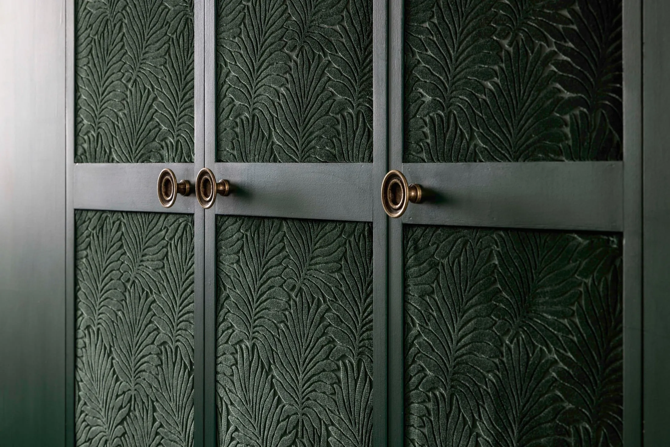 Placard aux portes tendues d'un tissu à motif de palmes vert, poignées en laiton